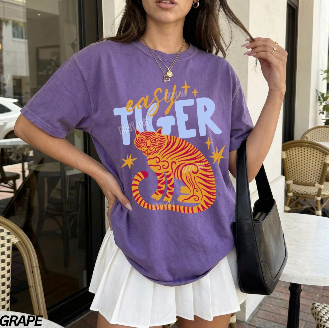 Person wearing a purple t-shirt with a tiger graphic and text, standing outdoors.