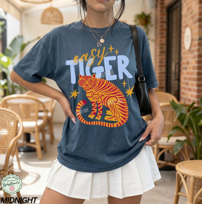 Person wearing a blue t-shirt with a tiger graphic and text in an outdoor setting.