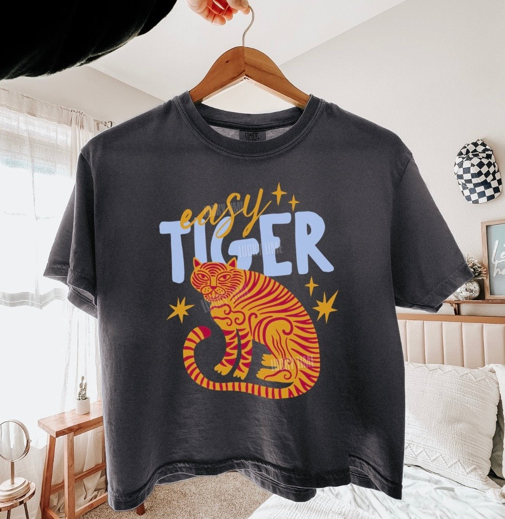 Black t-shirt with a tiger graphic and 'easy tiger' text on a hanger in a room.