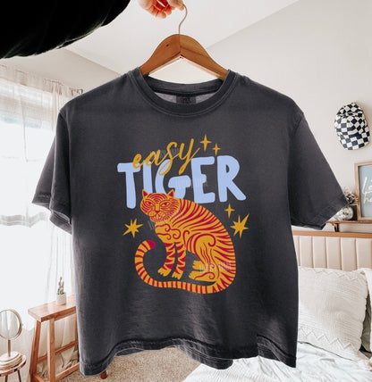 Black t-shirt with a tiger graphic and 'easy tiger' text on a hanger in a room.