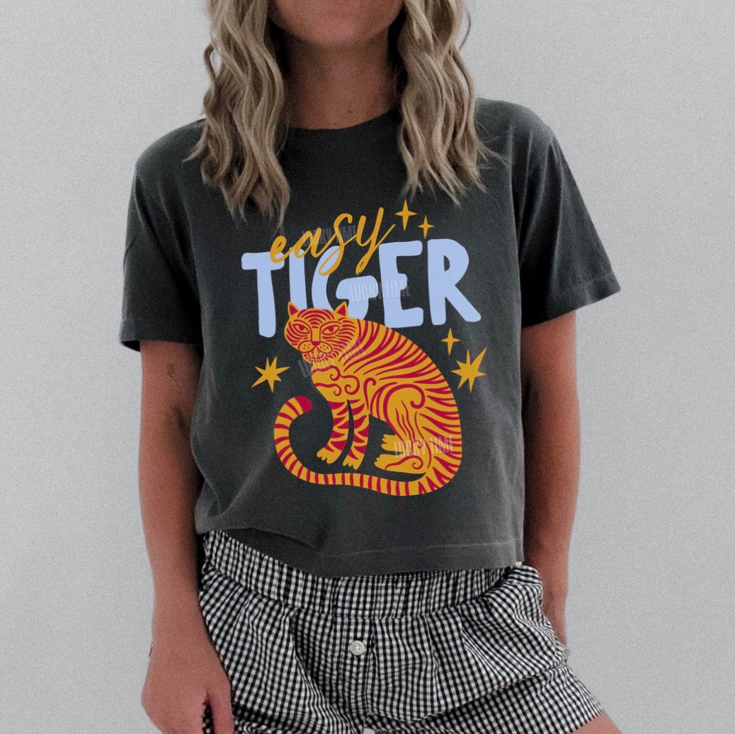 Person wearing a dark gray t-shirt with a tiger graphic and 'easy tiger' text, paired with checkered shorts on a plain background.