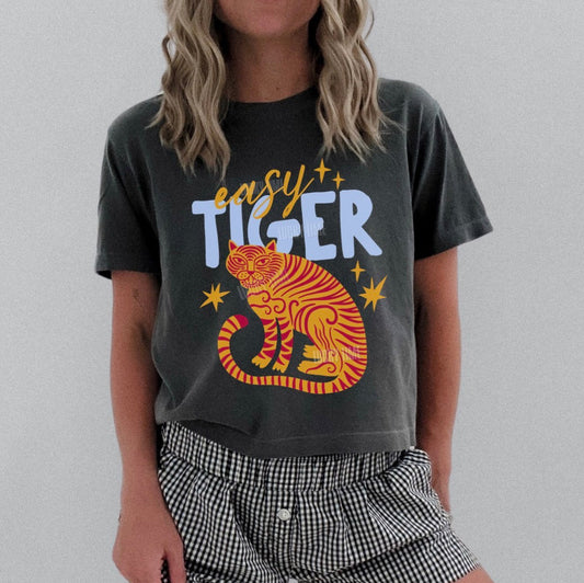Person wearing a dark gray t-shirt with a tiger graphic and 'easy tiger' text, paired with checkered shorts on a plain background.