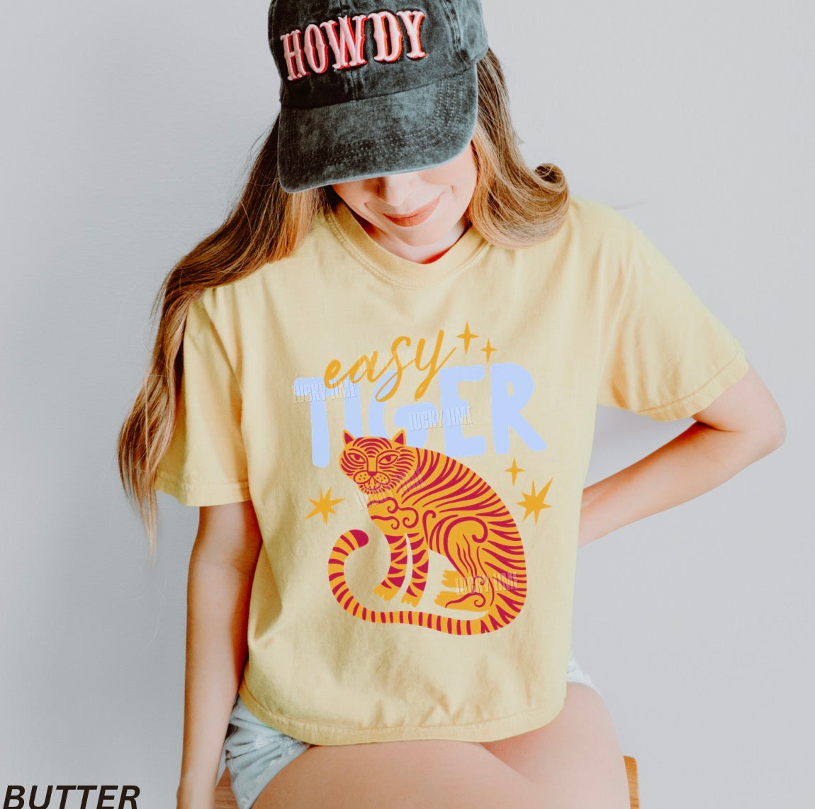 Person wearing a yellow t-shirt with a tiger graphic and 'easy tiger' text, paired with a 'HOWDY' cap.
