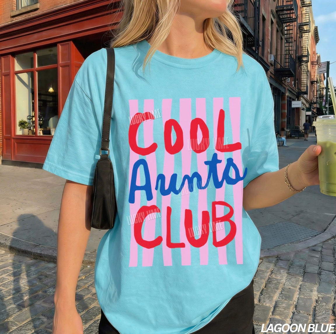 Woman wearing and lagoon blue colored shirt with pink striped design that says “cool aunts club”