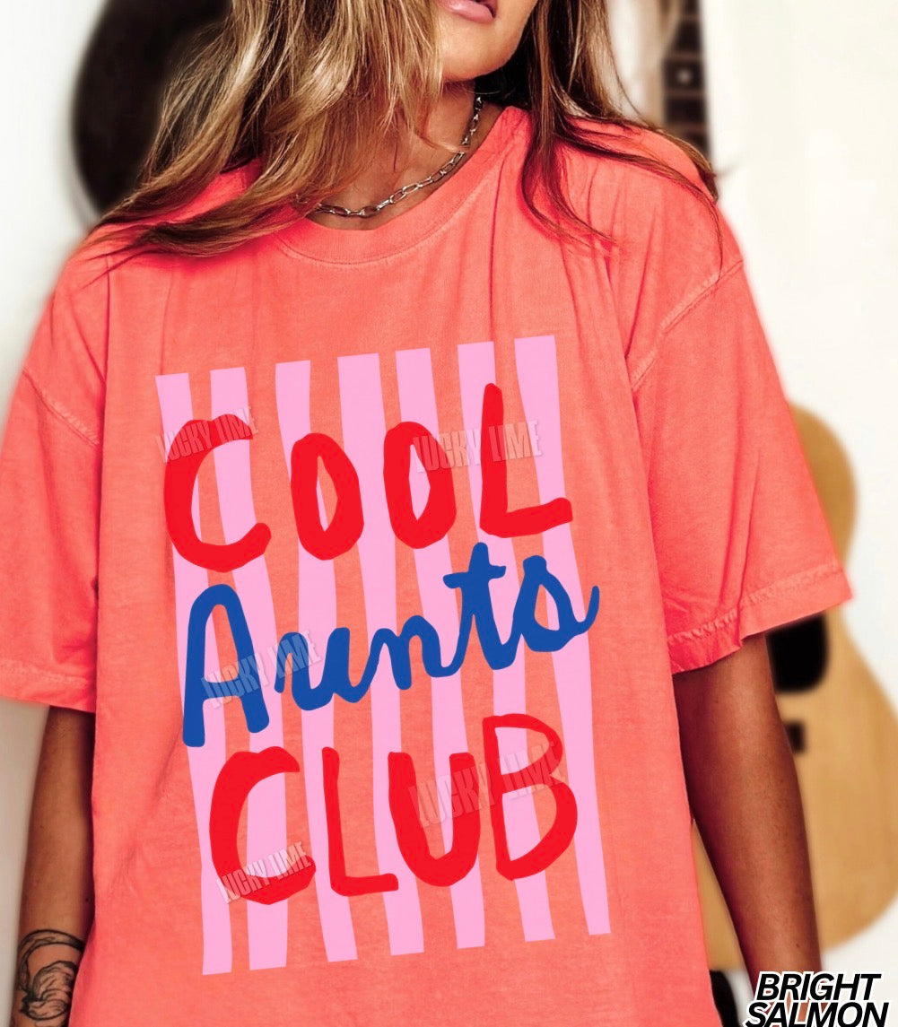 Woman wearing and bright salmon colored shirt with pink striped design that says “cool aunts club”