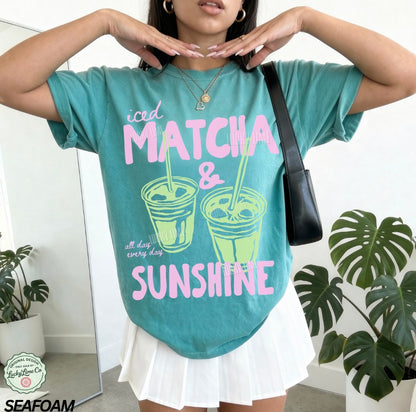 Person wearing a teal t-shirt with 'iced matcha & sunshine' text, standing indoors with plants in the background.
