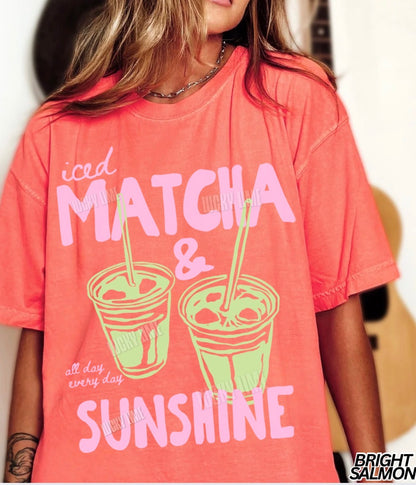 Person wearing a pink t-shirt with 'iced matcha & sunshine' text and graphics.