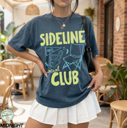 Person wearing a blue t-shirt with 'Sideline Social Club' design in a casual setting.