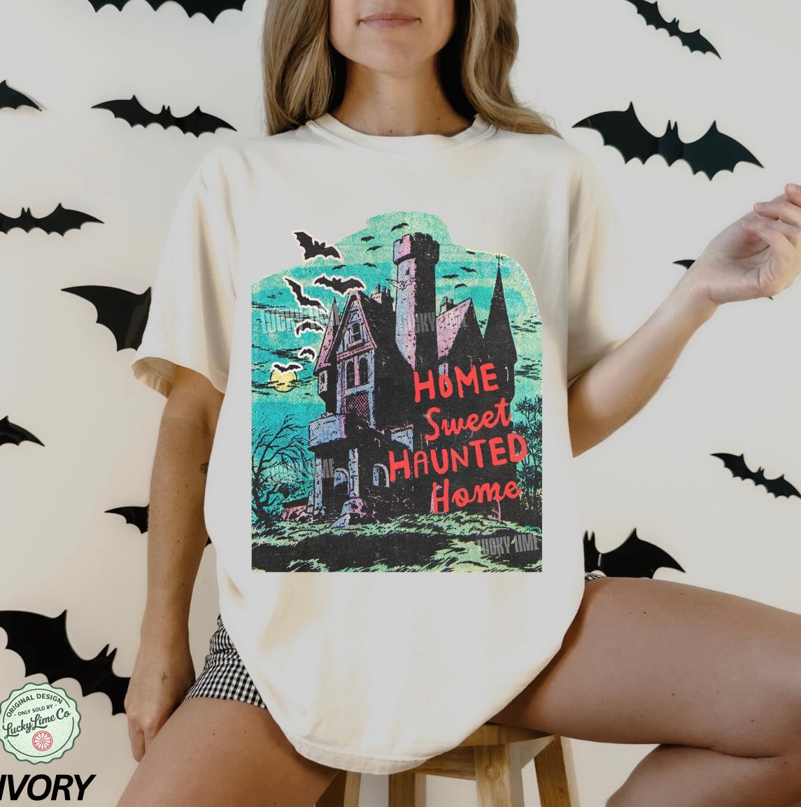 Person wearing a t-shirt with a haunted house design and 'Home Sweet Haunted Home' text, surrounded by bats.