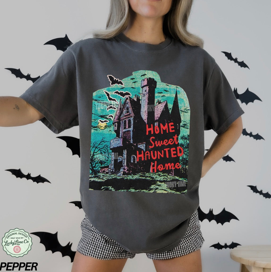 Person wearing a t-shirt with a haunted house design and 'Home Sweet Haunted Home' text, surrounded by bats.