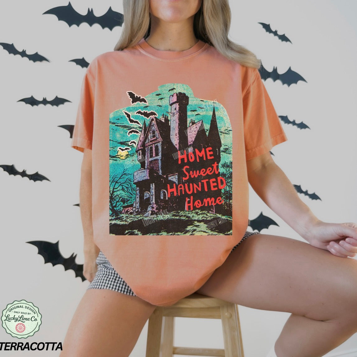 Person wearing a terracotta-colored t-shirt with a Halloween-themed design featuring a haunted house.