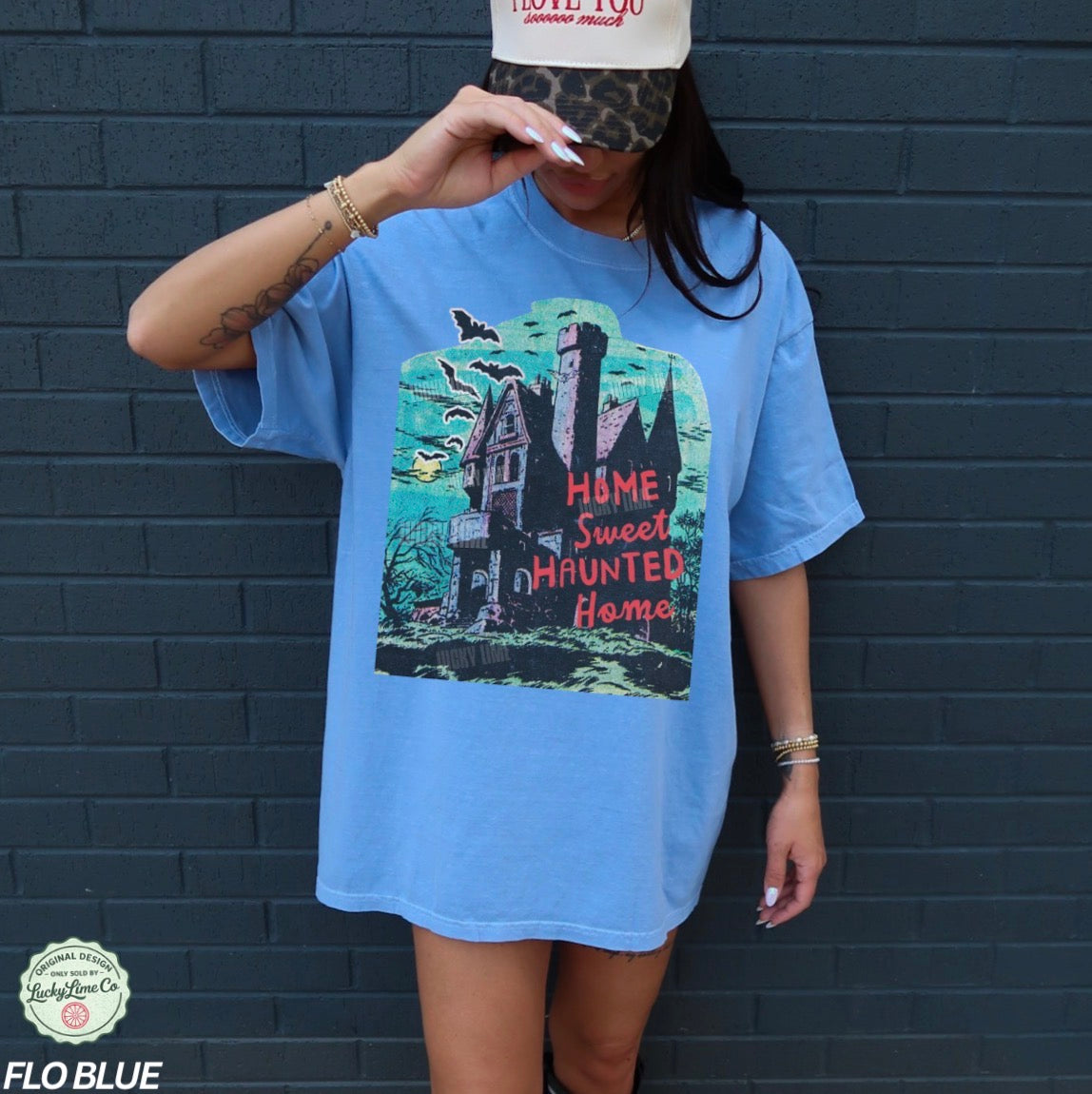 Person wearing a blue t-shirt with a haunted house graphic against a dark brick wall.
