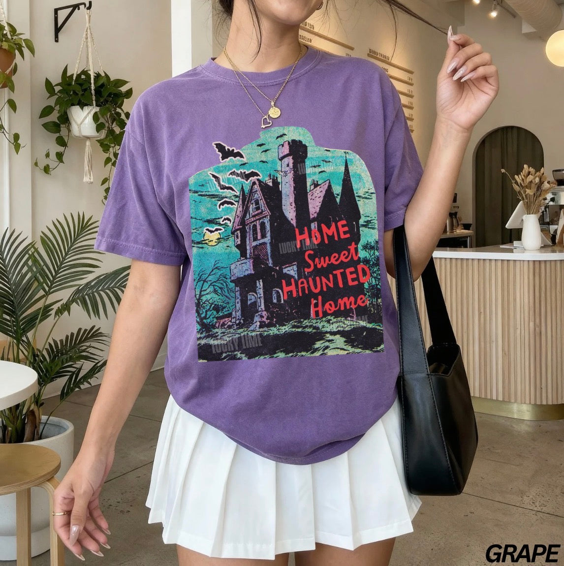 Person wearing a purple t-shirt with a haunted house design in an indoor setting.