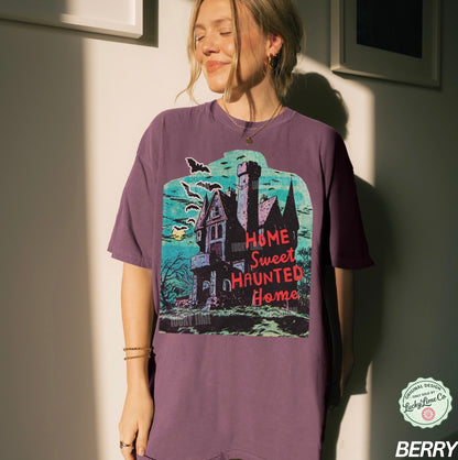 Person wearing a purple t-shirt with a haunted house design, standing against a neutral wall.