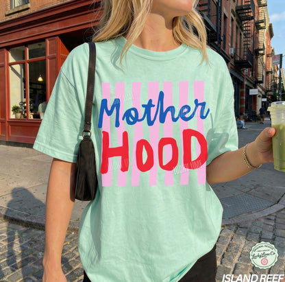 Person wearing a light green t-shirt with 'Mother Hood' print on a street.