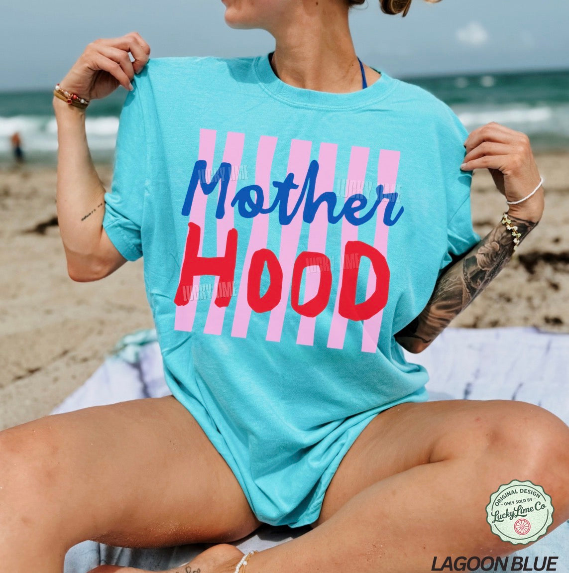Person wearing a light blue t-shirt with 'Mother Hood' print on a beach.