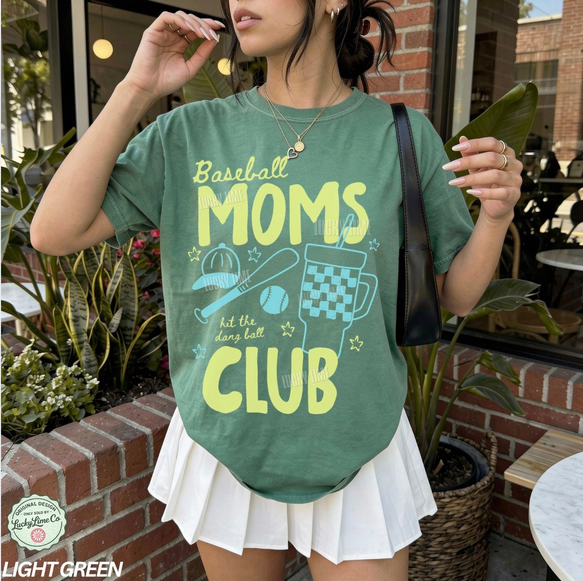 Person wearing a green t-shirt with 'Baseball Moms Club' text and graphics outdoors.