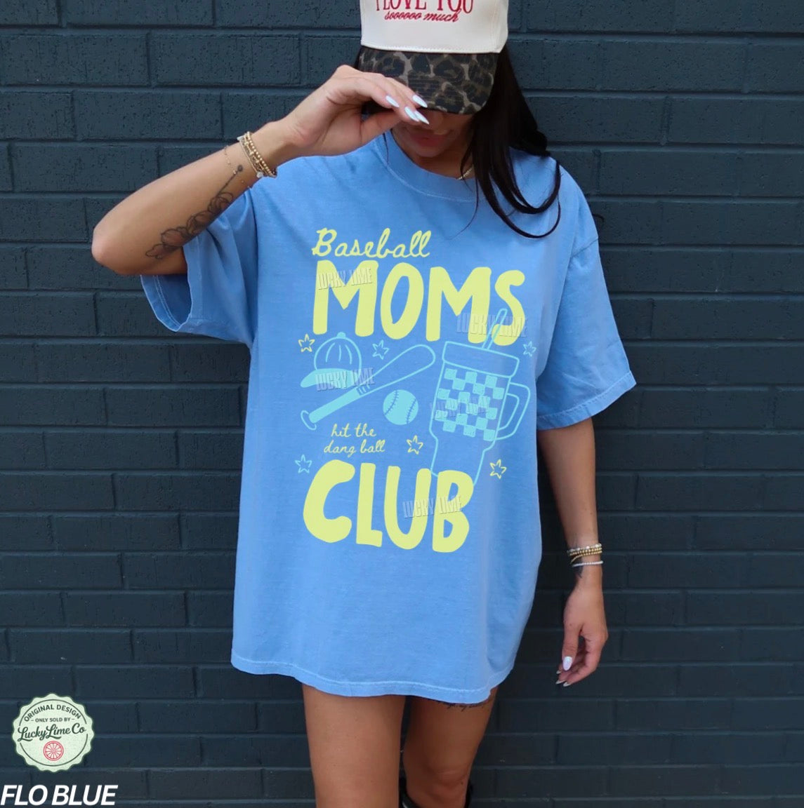 Person wearing a blue t-shirt with 'Baseball Moms Club' text against a dark brick wall.