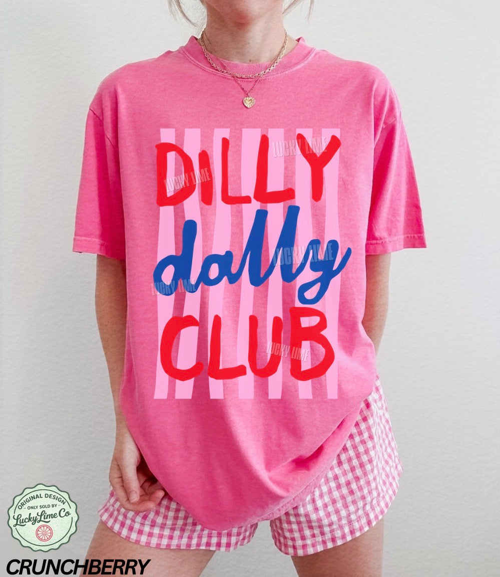 Person wearing a pink t-shirt with 'Dilly Dally Club' text and pink checkered shorts on a plain background.