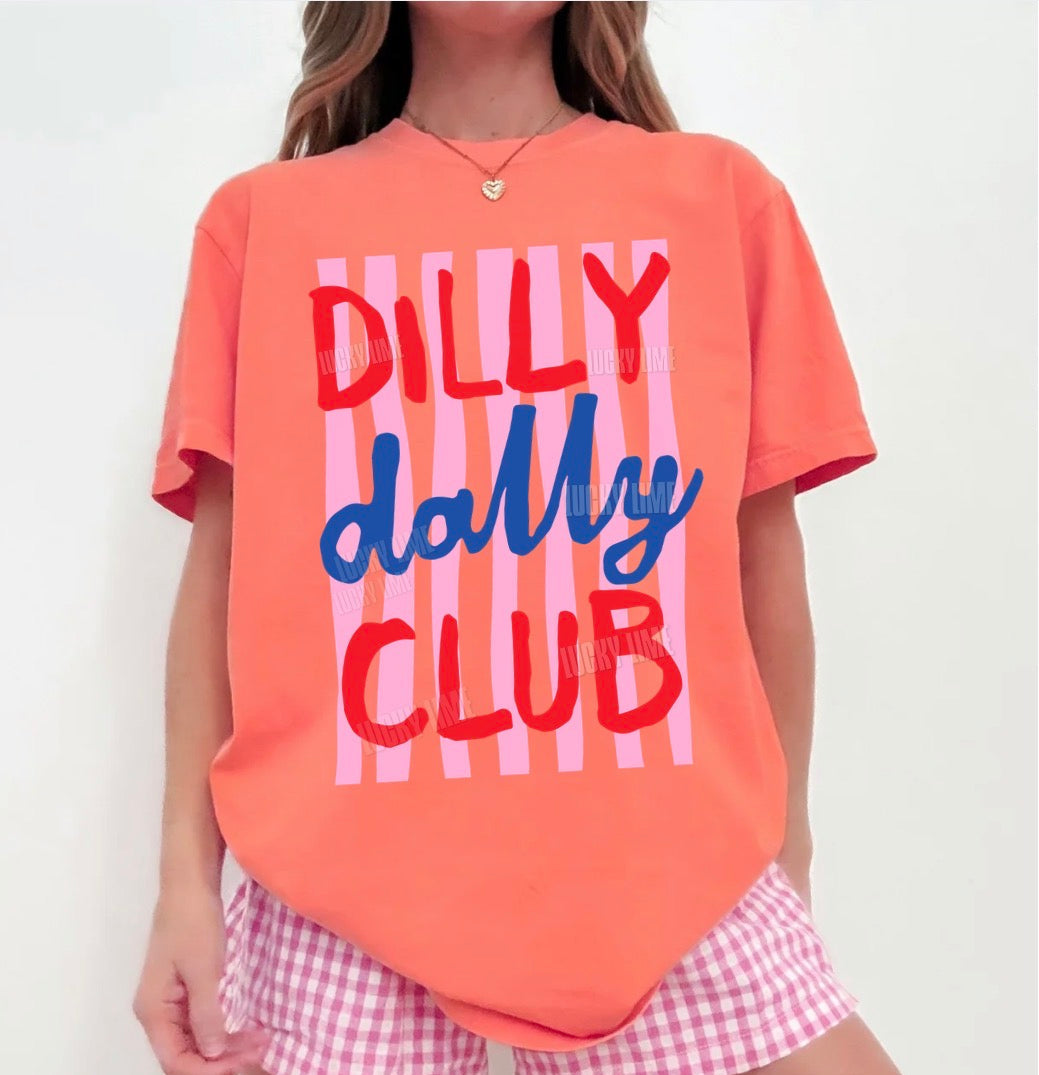 Person wearing a bright salmon t-shirt with 'Dilly Dally Club' text and pink checkered shorts.