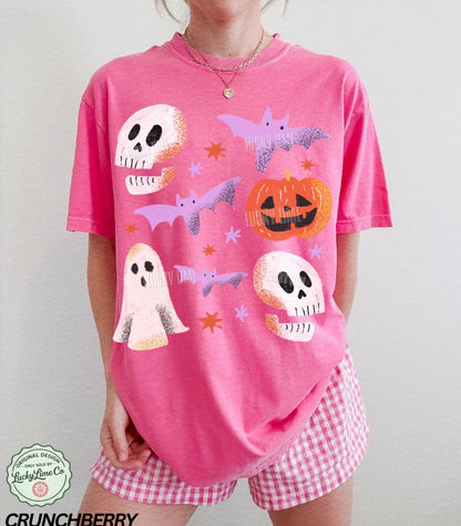 Person wearing a pink Halloween-themed t-shirt with ghosts, bats, and pumpkins on a plain background.