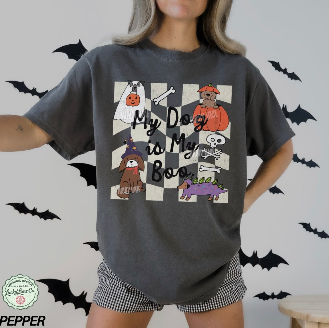 Person wearing a dark gray t-shirt with Halloween-themed dog illustrations and text, standing against a light gray background with black bats.