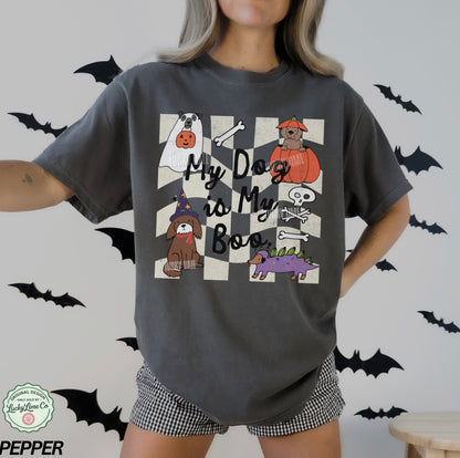 Person wearing a dark gray t-shirt with Halloween-themed dog illustrations and text, standing against a light gray background with black bats.