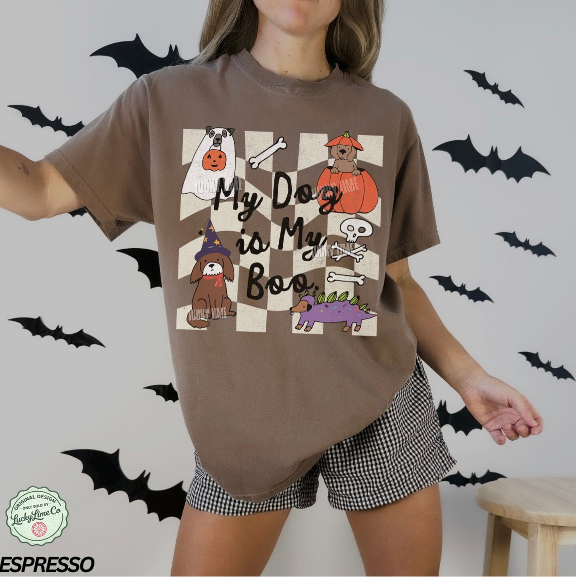 Person wearing a brown t-shirt with Halloween-themed design and checkered shorts, surrounded by black bats.
