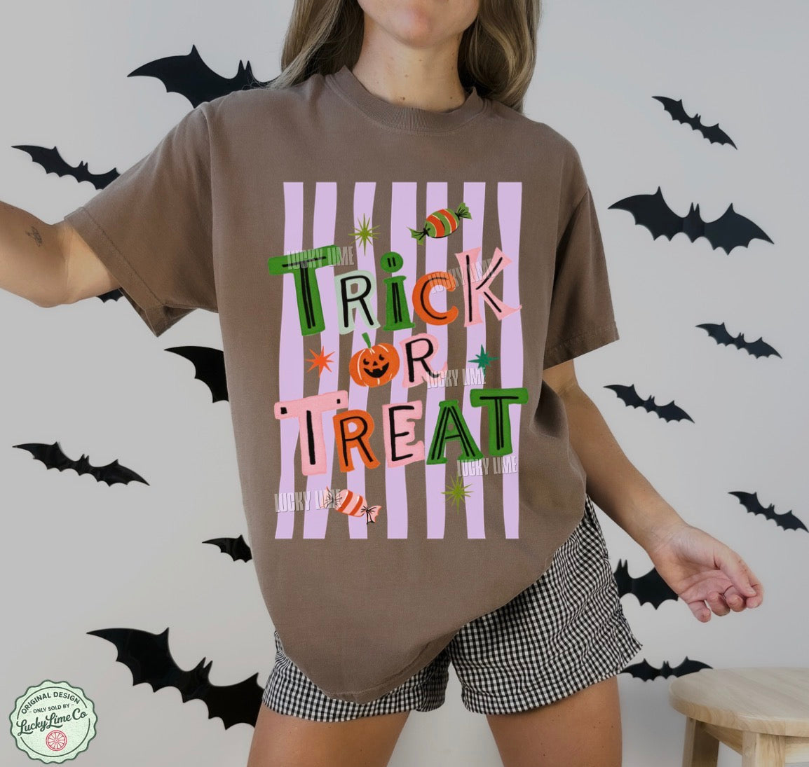 Person wearing a brown t-shirt with 'Trick or Treat' design, standing against a wall with black bats.
