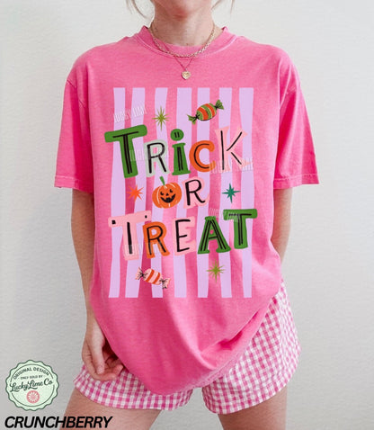 Person wearing a pink 'Trick or Treat' shirt with candy graphics on a plain background