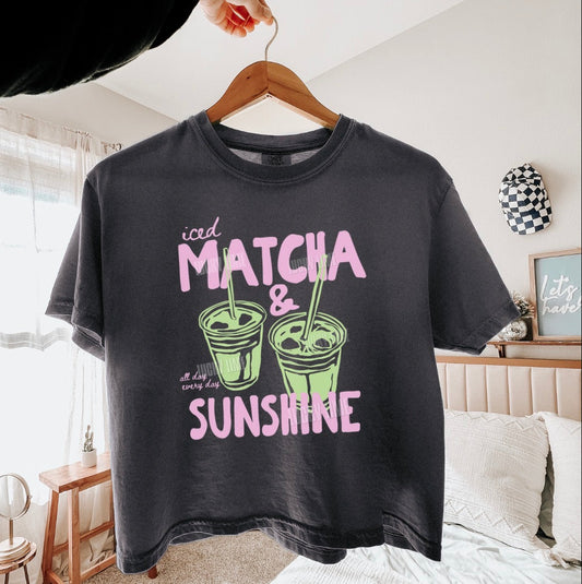Pepper t-shirt with matcha and sunshine graphic on a hanger in a room.