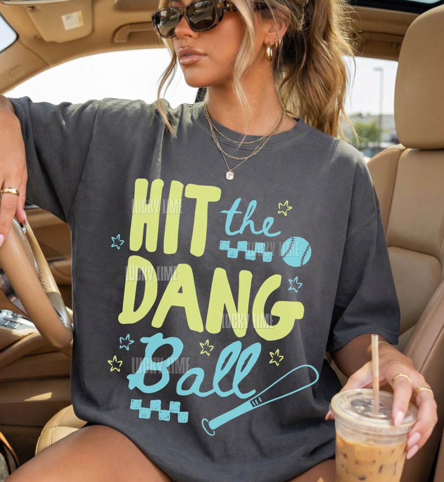 Woman wearing a dark grey tshirt with the words “Hit the Dang ball” with baseball graphics