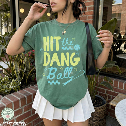 Woman wearing a green tshirt with the words “Hit the Dang ball” with baseball graphics