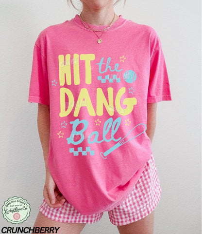 Woman wearing a dark pink tshirt with the words “Hit the Dang ball” with baseball graphics