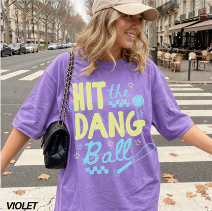Woman wearing a violet tshirt with the words “Hit the Dang ball” with baseball graphics
