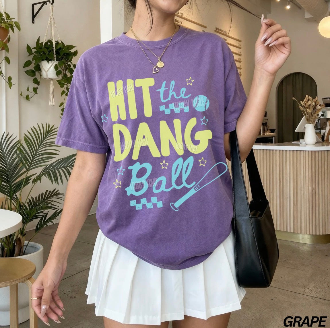 Woman wearing a grape colored tshirt with the words “Hit the Dang ball” with baseball graphics