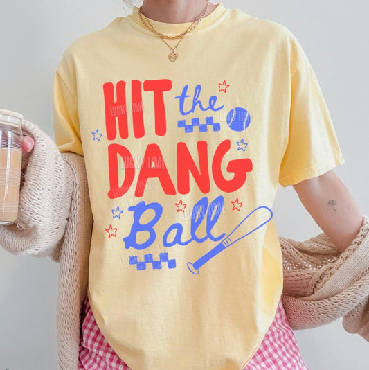 Person wearing a yellow t-shirt with colorful text and red checkered shorts, holding a drink.