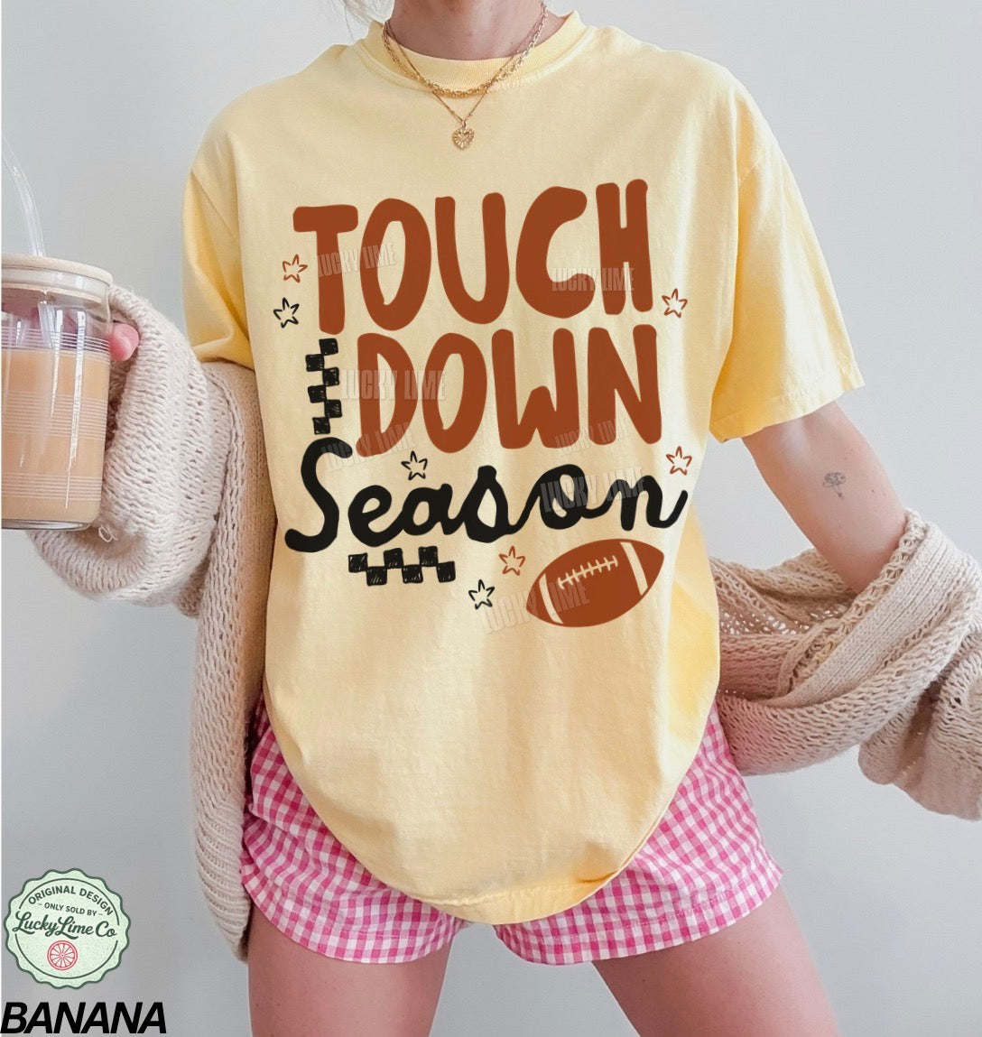 Person wearing a 'Touchdown Season' t-shirt with pink shorts and holding a drink.