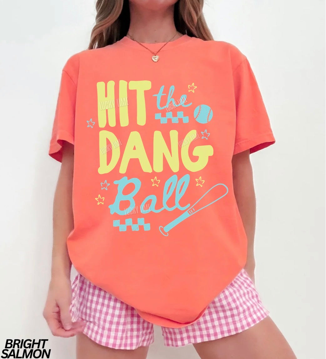 Woman wearing a bright salmon tshirt with the words “Hit the Dang ball” with baseball graphics