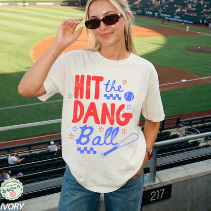 Woman wearing a t-shirt with 'Hit the Dang Ball' text at a baseball stadium.