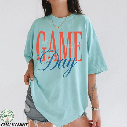 Person wearing a light blue t-shirt with 'Game Day' text in red and blue.