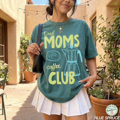 Woman wearing a teal t-shirt with 'tired moms coffee club' design outdoors.