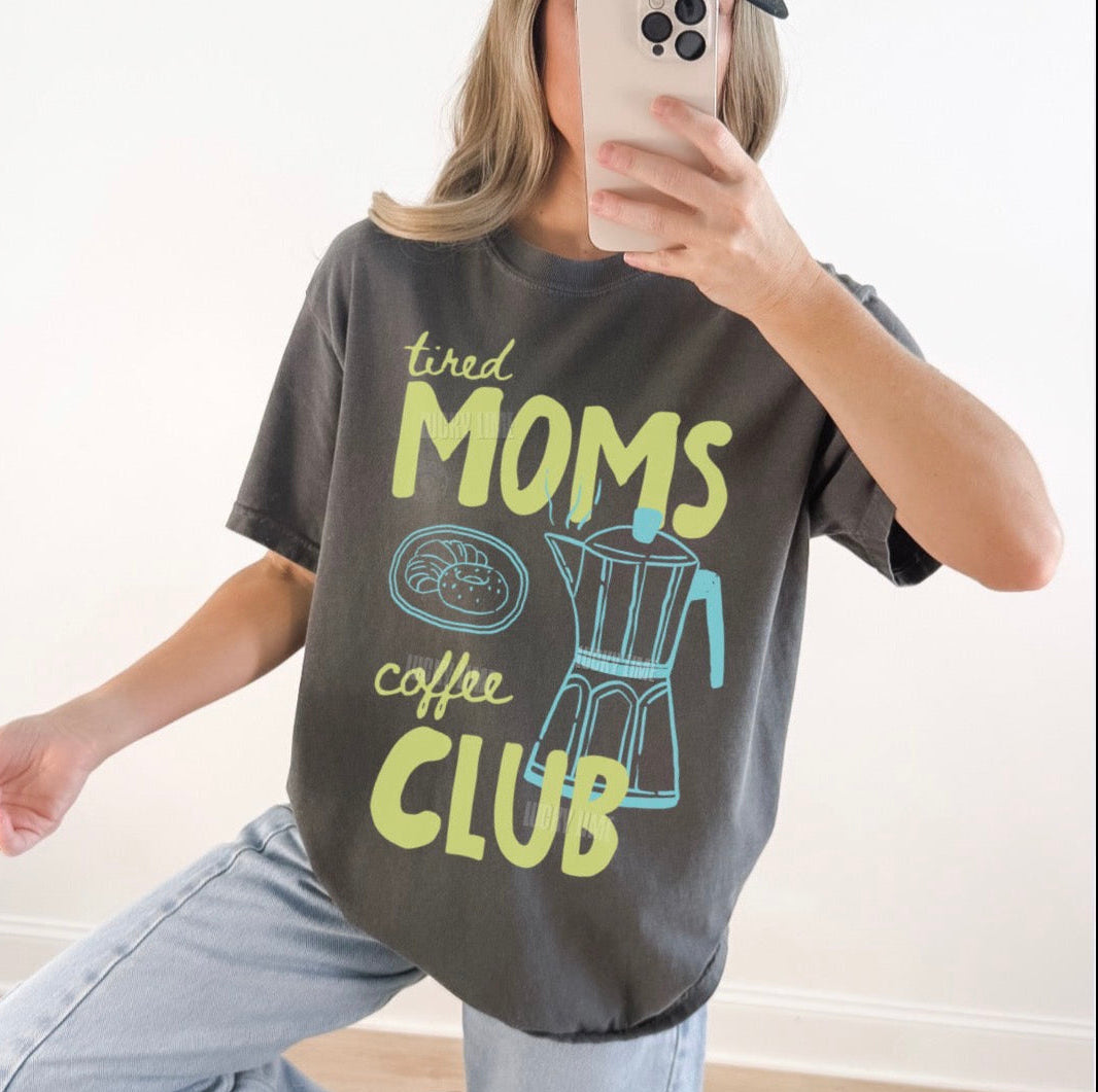 Person wearing a t-shirt with 'tired moms coffee club' text and graphics.