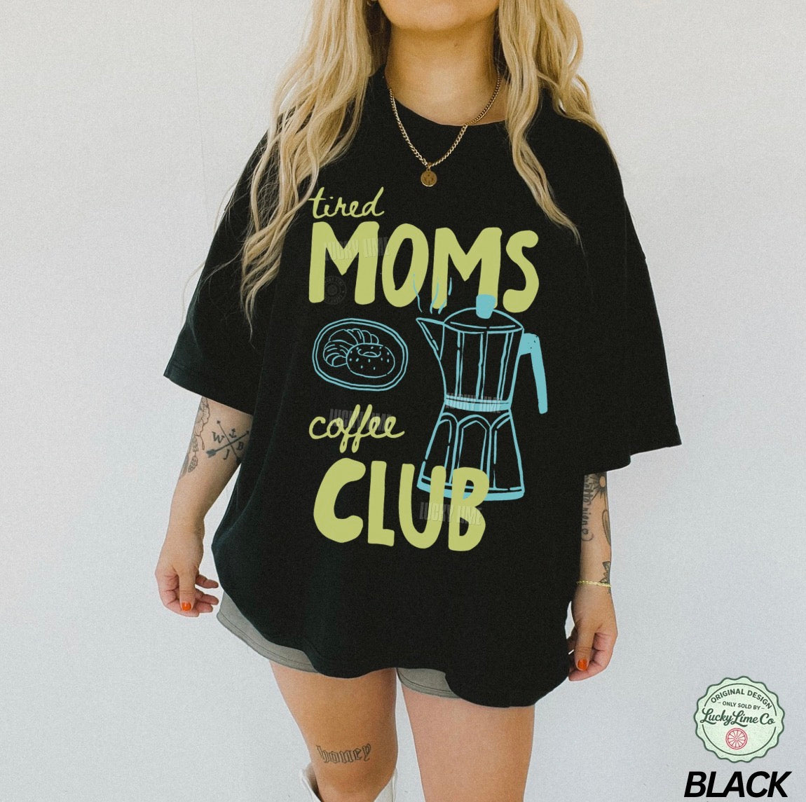 Person wearing a black t-shirt with 'tired moms coffee club' text and graphics on a plain background