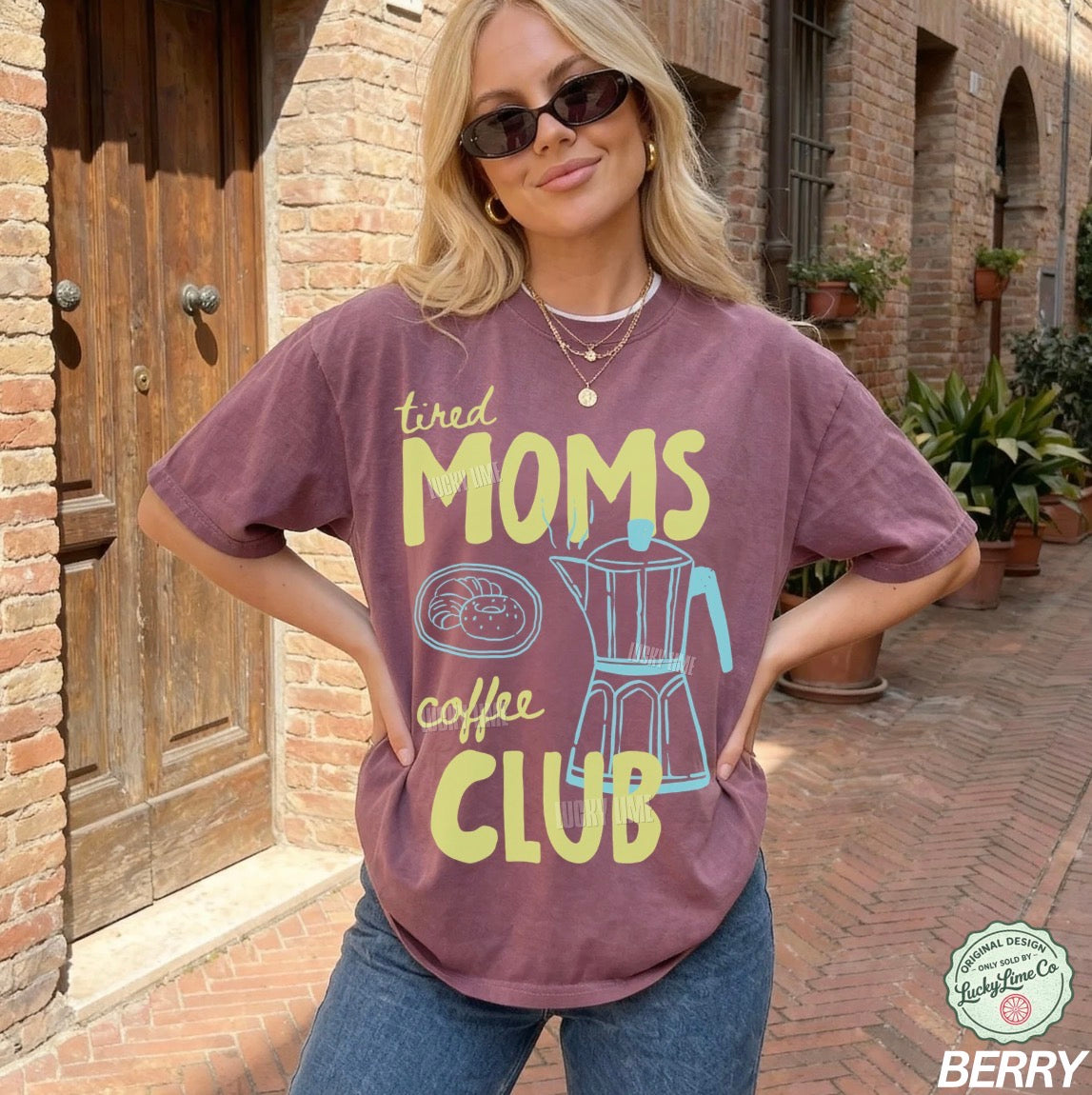 Woman wearing a 'tired moms coffee club' t-shirt in front of a brick building.