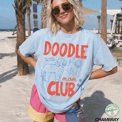 Person wearing a 'Doodle Mom Club' t-shirt on a beach