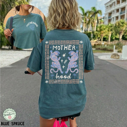 Person wearing a teal t-shirt with 'Motherhood' design outdoors.