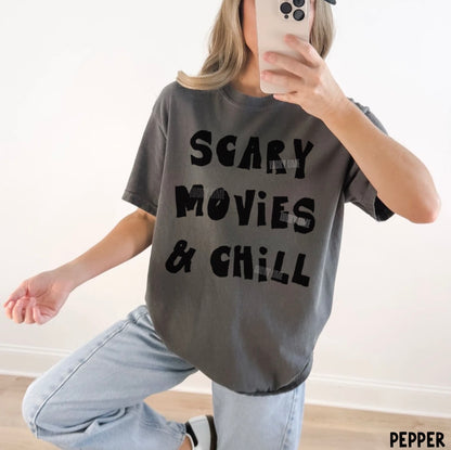 Person wearing a gray t-shirt with 'SCARY MOVIES & CHILL' text, taking a mirror selfie.
