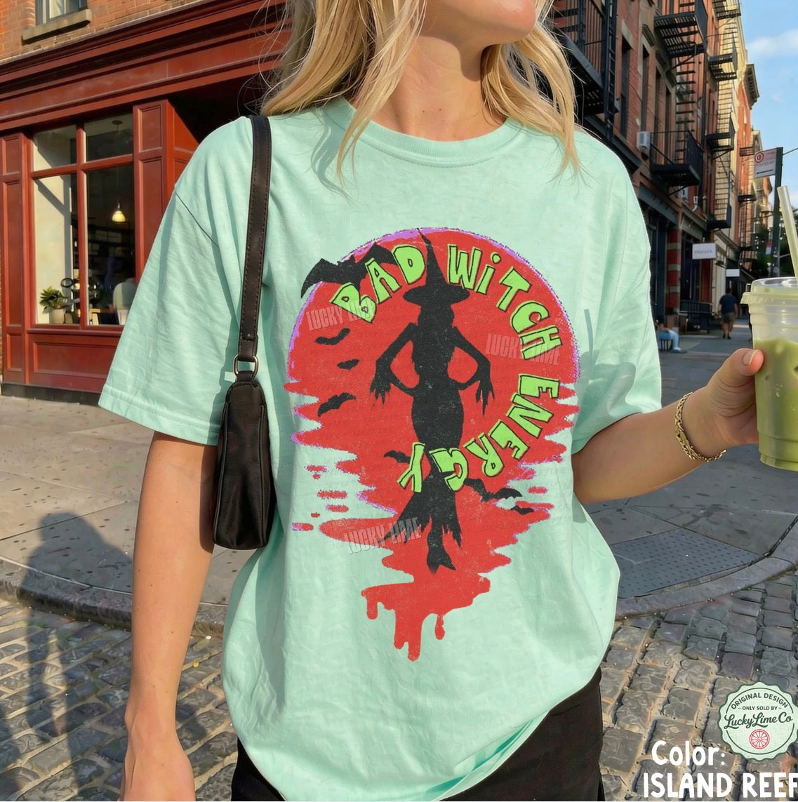 Person wearing a light green t-shirt with a colorful graphic design on a city street.