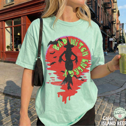 Person wearing a light green t-shirt with a colorful graphic design on a city street.